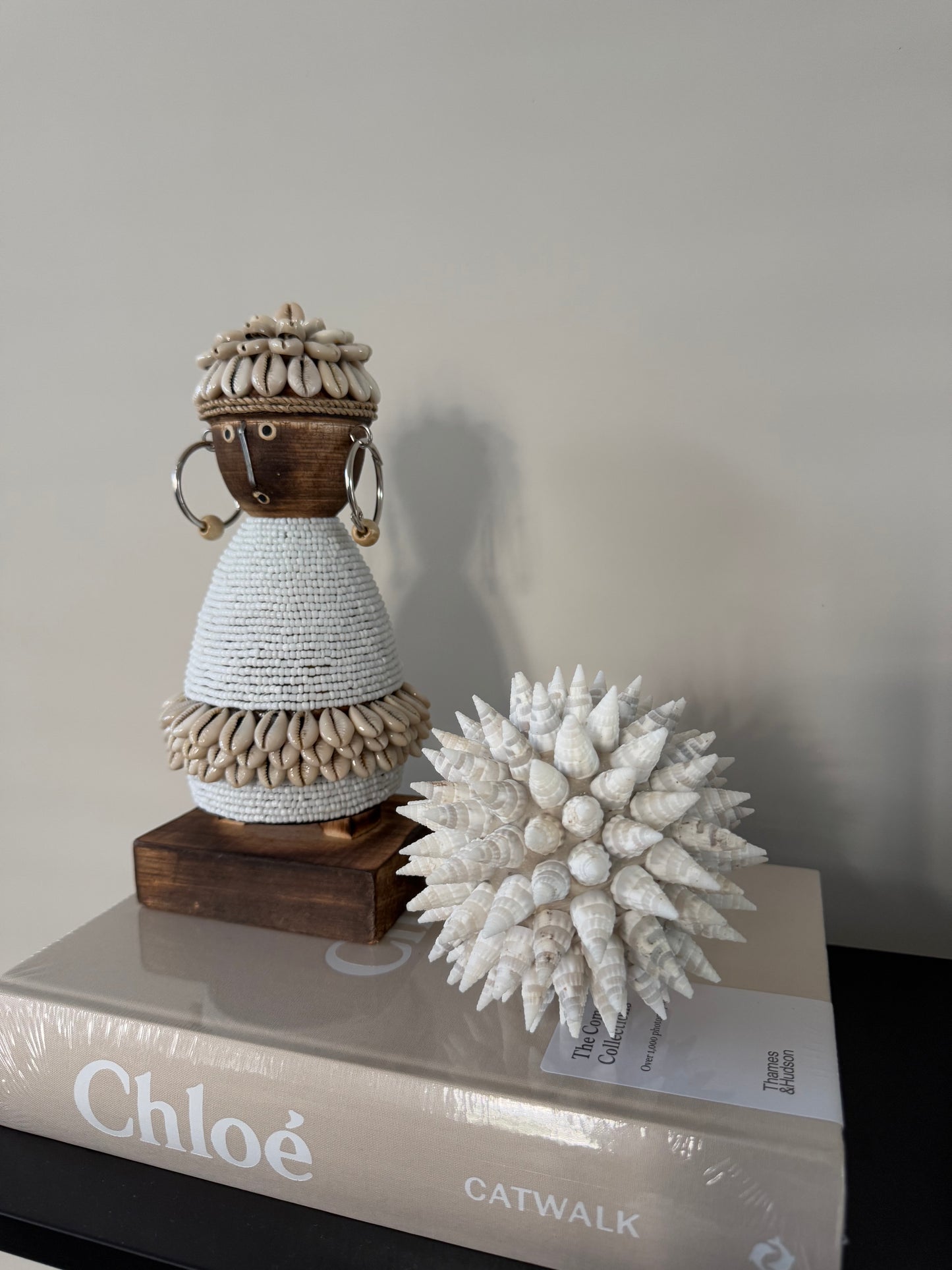 Handgemaakte Namji Doll houten pop van circa 25 cm, versierd met witte glaskralen, kauri schelpen en oorbellen, uniek cultureel decoratiestuk