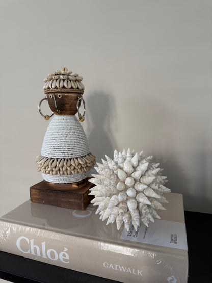 Handgemaakte Namji Doll houten pop van circa 25 cm, versierd met witte glaskralen, kauri schelpen en oorbellen, uniek cultureel decoratiestuk